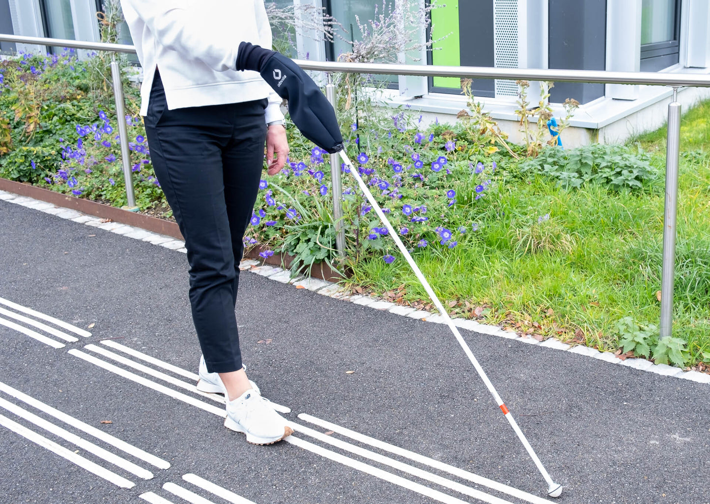 Frau mit weissem Stock und obvita Stockmuff auf Gehweg